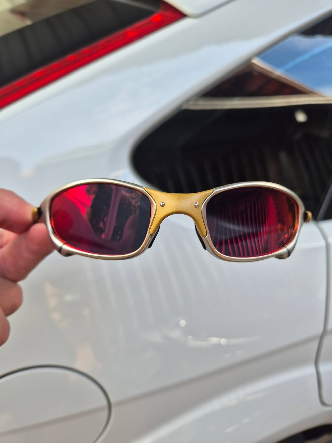Óculos Juliet com lente rubi em frente a um carro branco